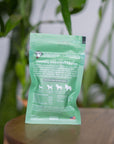 back of mini green colored bag of regular strength lolahemp calming hemp soft chews on wooden table with plants in the background