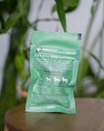 back of mini green colored bag of regular strength lolahemp hip & joint hemp soft chews on wooden table with plants in the background