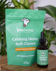 Green colored bag of regular strength lolahemp calming hemp soft chews with brown 600mg regular strength lolahemp oil bottle with green label on wooden table with plants in the background