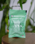 back of mini green colored bag of regular strength lolahemp calming hemp soft chews on wooden table with plants in the background